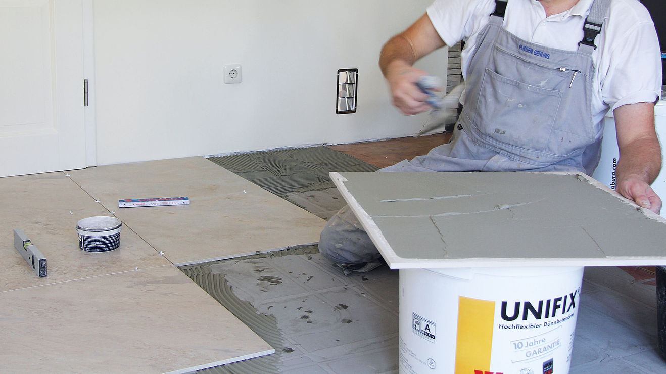 Auftragen einer rückseitigen Kontaktschicht Handwerker bestreicht Fliese